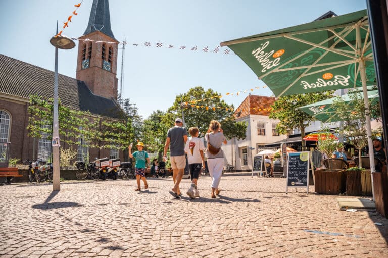 Mensen lopen op een zonnige dag over het kerkplein in Zandvoort, met een terras en de kerk op de achtergrond.