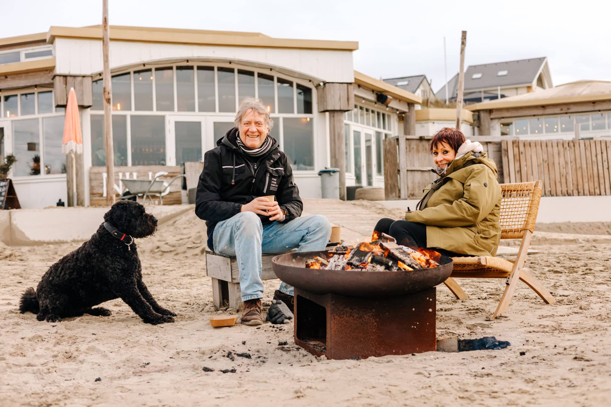 Een stel en een hond op het strand in de winter buiten bij een kampvuur